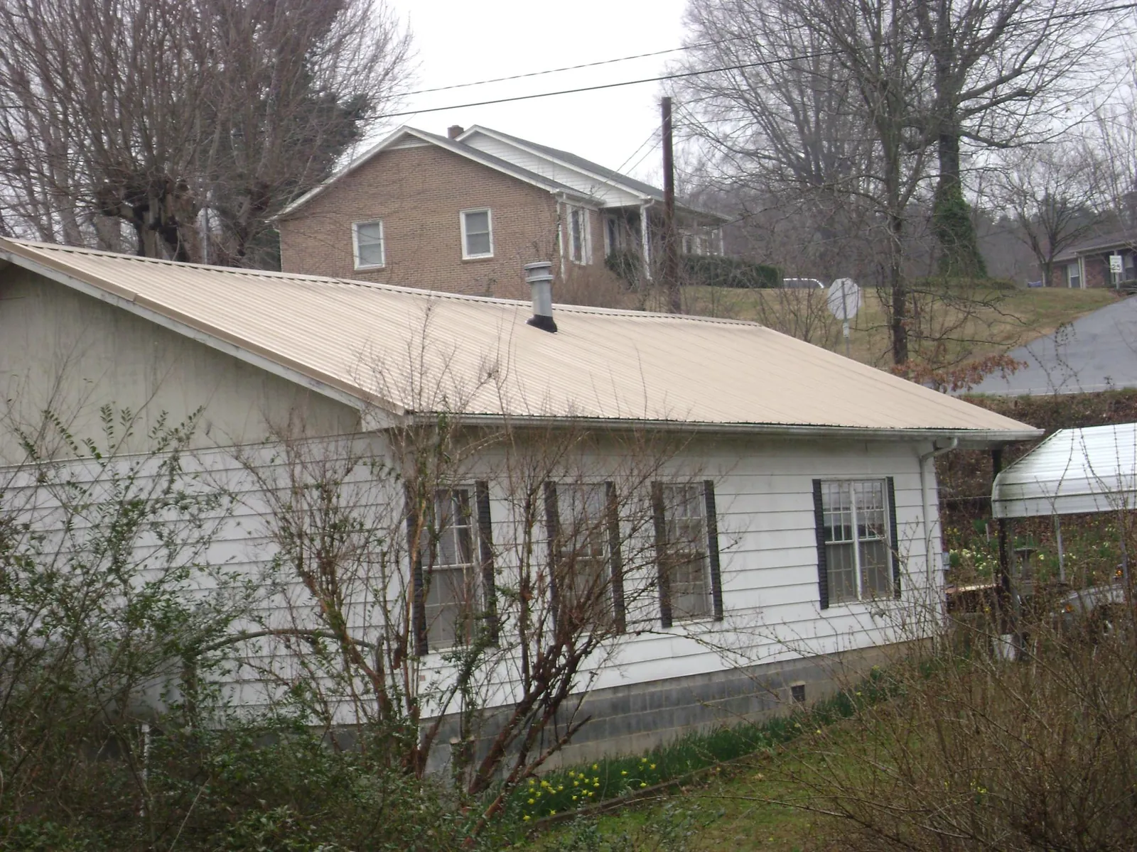 Tan metal roof on a white sided house set into a hillside — Commercial Roofing by Roofing Brothers in Danbury